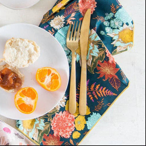 Table setting with pastries, coffee, and fruit on a white surface with colorful napkins.